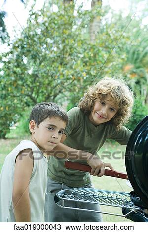 Stock Image - Two boys standing next to barbecue, looking at camera. Fotosearch