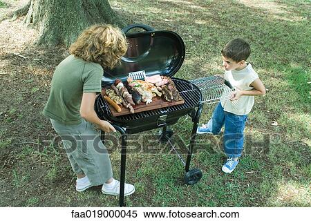 Stock Photography - Two boys standing next to tray of grilled meat on barbecue. Fotosearch