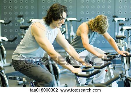 Two men riding exercise bikes View Large Photo Image Stock Image - Two men riding exercise bikes. Fotosearch