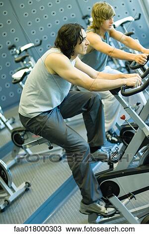 Stock Image - Two men riding exercise bikes. Fotosearch