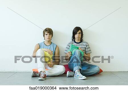 Two teen boys sitting on floor, holding cushions View Large Photo Image Picture - Two teen boys sitting on floor, holding cushions. Fotosearch