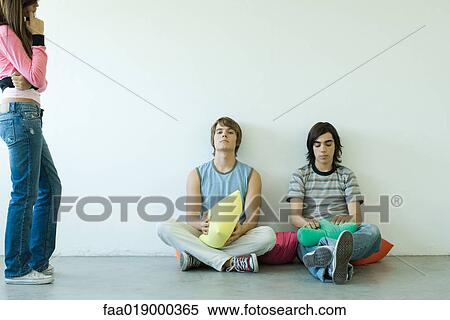 Two teen boys sitting on floor while teen girl stands nearby View Large Photo Image Stock Photography - Two teen boys sitting on floor while teen girl stands nearby. Fotosearch
