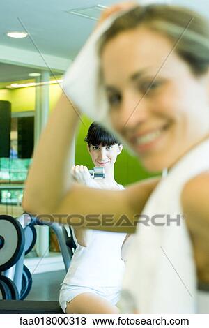 Stock Photo - Two women in weight room, woman in foreground with towel around neck. Fotosearch