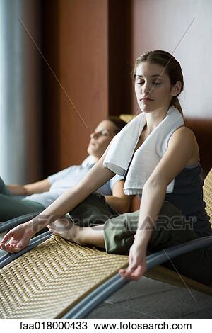 Stock Image - Two women relaxing on lounge chairs, one sitting indian style . Fotosearch