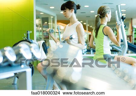 Picture - Two women working out in weight room. Fotosearch