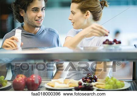 Stock Photograph - Two young adults standing at snackbar, chatting. Fotosearch