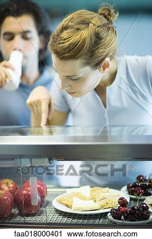 Two young adults standing, choosing healthy snack in cafeteria View Large Photo Image Stock Image - Two young adults standing, choosing healthy snack in cafeteria. Fotosearch