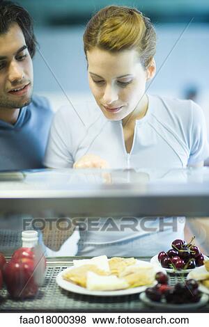 Two young adults standing, choosing healthy snack in cafeteria View Large Photo Image Stock Photo - Two young adults standing, choosing healthy snack in cafeteria. Fotosearch