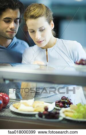 Two young adults standing, choosing healthy snack in cafeteria View Large Photo Image Stock Photo - Two young adults standing, choosing healthy snack in cafeteria. Fotosearch