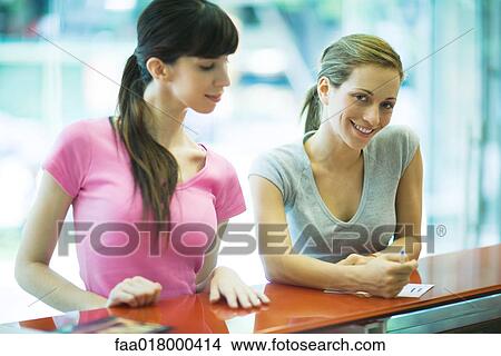 Two young women checking in at health club counter, waist up View Large Photo Image Picture - Two young women checking in at health club counter, waist up. Fotosearch