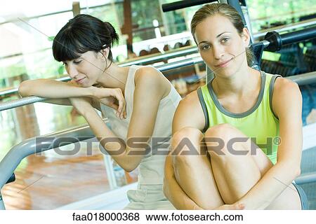 Stock Photo - Two young women sitting in weight room. Fotosearch