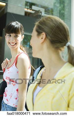 Two young women smiling at each other, smiling View Large Photo Image Stock Image - Two young women smiling at each other, smiling. Fotosearch