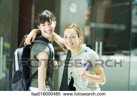 Stock Photography - Two young women standing together, one with hand around other's shoulder, holding bottle of water. Fotosearch