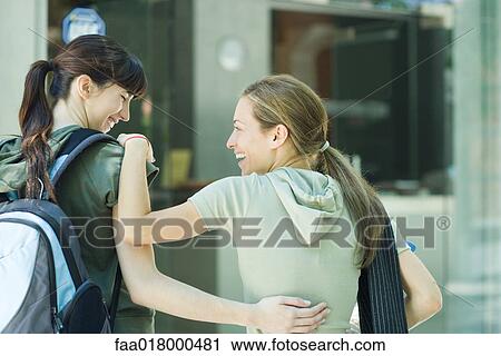 Stock Image - Two young women with arms around each other, laughing, rear view. Fotosearch