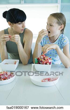 Woman and girl sitting side by side eating bowls of candy View Large Photo Image Stock Photo - Woman and girl sitting side by side eating bowls of candy. Fotosearch