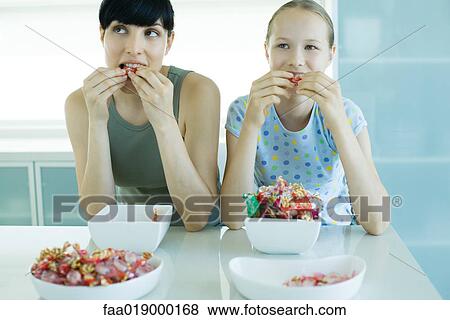 Woman and girl sitting side by side eating bowls of candy View Large Photo Image Stock Photo - Woman and girl sitting side by side eating bowls of candy. Fotosearch