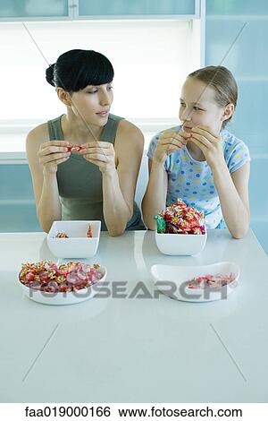 Woman and girl sitting side by side eating bowls of candy View Large Photo Image Stock Photograph - Woman and girl sitting side by side eating bowls of candy. Fotosearch