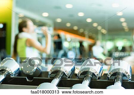 Woman drinking bottle of water, focus on rack of dumbbells in foreground View Large Photo Image Stock Image - Woman drinking bottle of water, focus on rack of dumbbells in foreground. Fotosearch