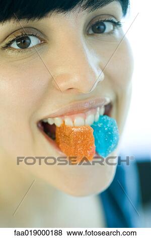 Stock Photo - Woman holding pieces of candy between teeth, smiling at camera. Fotosearch