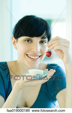 Stock Photo - Woman holding up fresh cherry in one hand and saucer with finger sandwiches in the other hand. Fotosearch