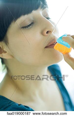 Woman holding up piece of candy to mouth, eyes half-closed View Large Photo Image Stock Photo - Woman holding up piece of candy to mouth, eyes half-closed. Fotosearch