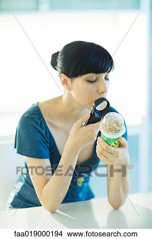 Picture - Woman looking at yogurt through magnifying glass. Fotosearch