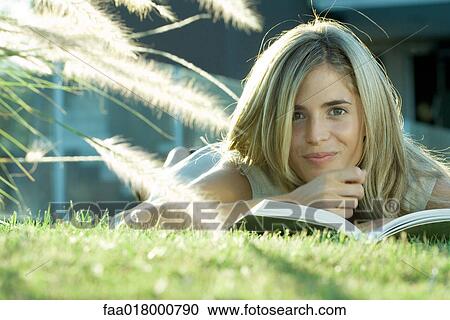 Woman lying in grass, reading book, smiling at camera View Large Photo Image Stock Image - Woman lying in grass, reading book, smiling at camera. Fotosearch