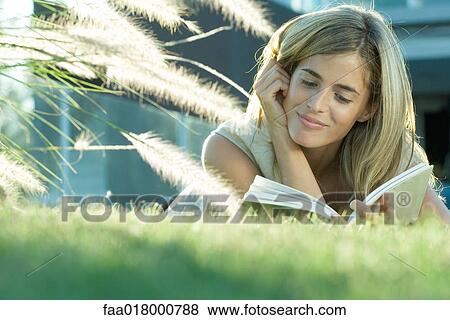 Stock Photo - Woman lying in grass, reading book. Fotosearch