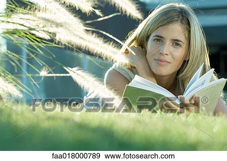 Woman lying in grass, reading book, smiling at camera View Large Photo Image Stock Photo - Woman lying in grass, reading book, smiling at camera. Fotosearch