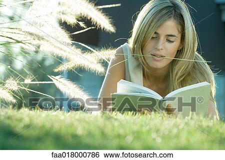 Stock Photograph - Woman lying in grass, reading book. Fotosearch