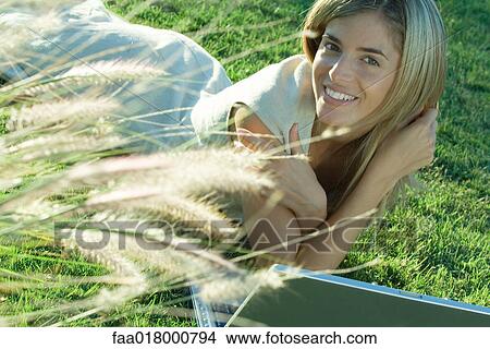 Picture - Woman lying in grass, using laptop. Fotosearch
