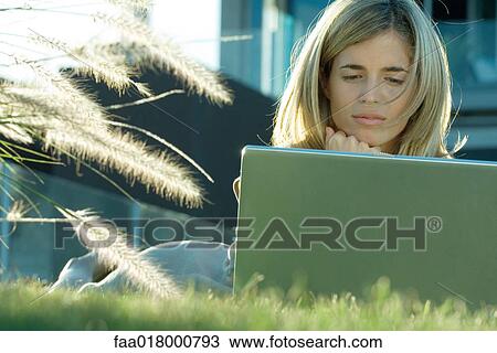 Woman lying in grass, using laptop View Large Photo Image Stock Image - Woman lying in grass, using laptop. Fotosearch