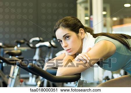 Stock Image - Woman on exercise bike, leaning forward, resting on handle bars. Fotosearch