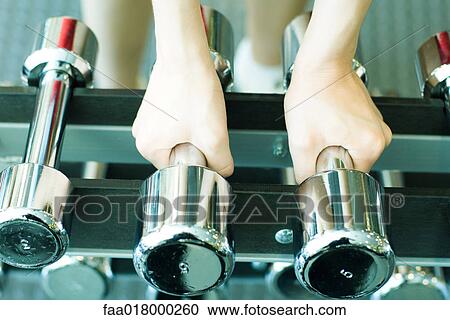 Stock Image - Woman picking up dumbbells. Fotosearch