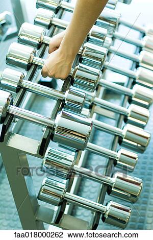 Stock Image - Woman picking up dumbbells. Fotosearch