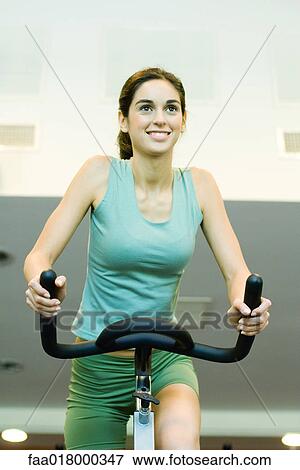 Stock Photo - Woman riding exercise bike. Fotosearch