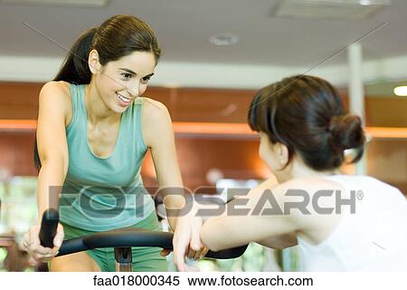 Woman riding exercise bike, talking to second woman View Large Photo Image Stock Photography - Woman riding exercise bike, talking to second woman. Fotosearch