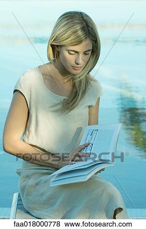 Stock Photo - Woman sitting and reading book, water in background. Fotosearch