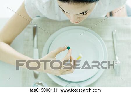 Stock Image - Woman sitting at empty plate holding vitamin. Fotosearch