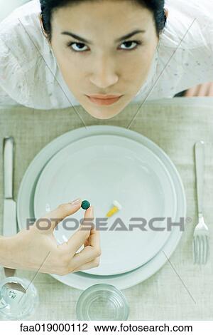 Woman sitting at empty plate holding vitamin, looking up at camera View Large Photo Image Stock Image - Woman sitting at empty plate holding vitamin, looking up at camera. Fotosearch