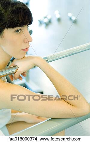 Woman sitting in weight room, holding on to metal bar, looking away View Large Photo Image Picture - Woman sitting in weight room, holding on to metal bar, looking away. Fotosearch