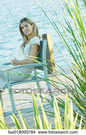 Woman sitting on dock with book on lap, looking at camera View Large Photo Image Picture - Woman sitting on dock with book on lap, looking at camera. Fotosearch