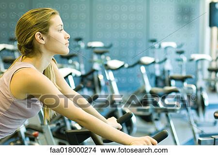 Picture - Woman sitting on stationary exercise bike. Fotosearch