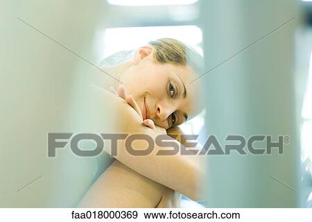 Stock Photo - Woman sitting with head on knees, smiling at camera, focus on background. Fotosearch