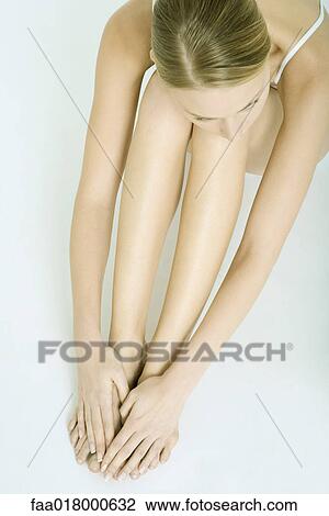 Stock Image - Woman sitting with knees up, hands over feet, view from directly above. Fotosearch