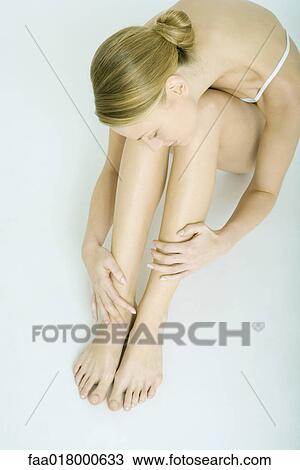 Stock Image - Woman sitting with knees up, touching legs, view from directly above. Fotosearch