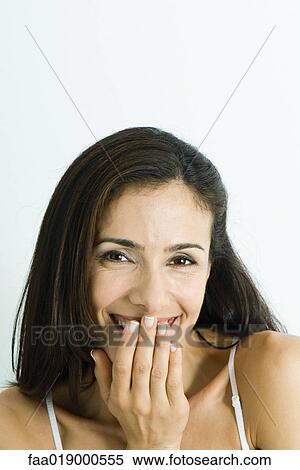 Stock Photography - Woman smiling and covering mouth, portrait. Fotosearch
