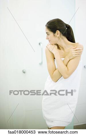 Stock Image - Woman standing wrapped in towel, hands on shoulders, looking away. Fotosearch
