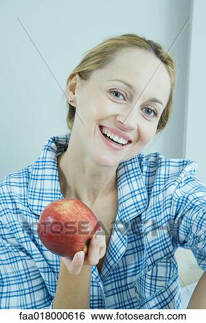 Stock Photograph - Woman wearing pajamas, holding up apple. Fotosearch