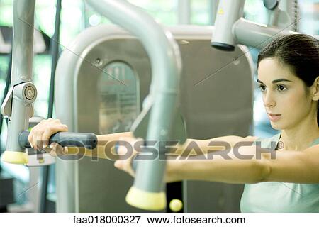 Stock Photo - Woman working out with weight machine. Fotosearch
